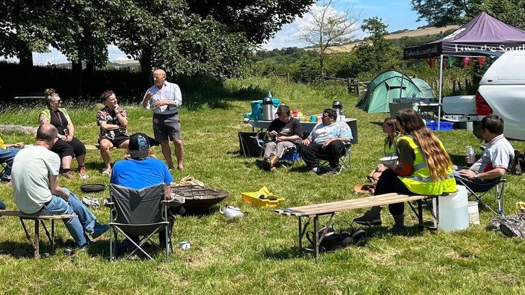 A photo of a group of people sat around a campfire listening to a talk